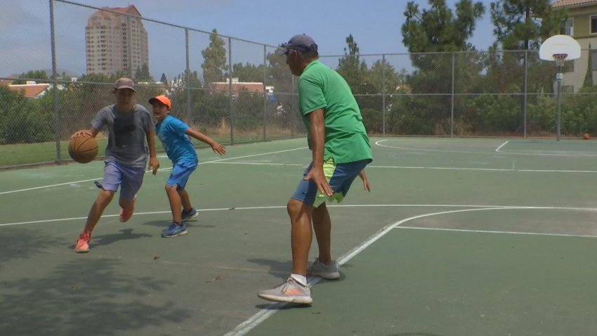 Two boys and a man play basketball on an outdoor court.