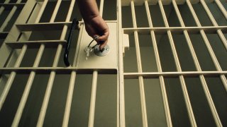 A hand turns a key in a jail cell door