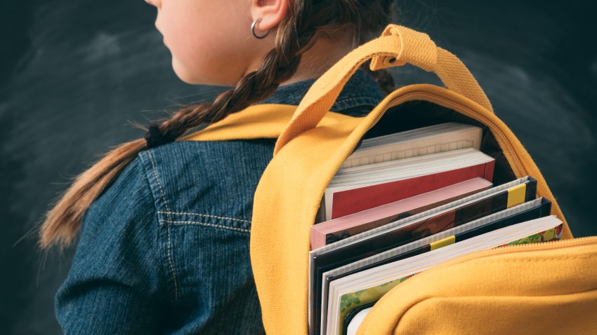 Back to school. Back view of young girl ready to study, with open backpack full with books.