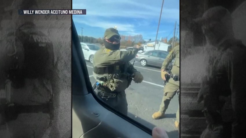 Foto de un agente enmascarado con una macana rompiendo el vidrio de un auto.